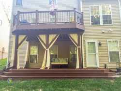 Two-story composite deck with upper railing, covered lower patio with curtains, and backyard seating area, built by a deck contractor near me in Charlotte, NC.